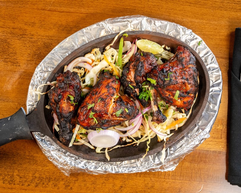 Tandoori chicken drumsticks and thighs with sliced onions, cabbage, and lime in a sizzling skillet.