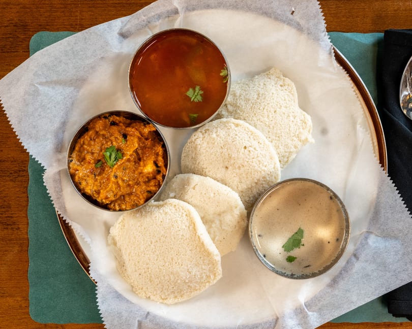Overhead view of a South Indian thali with idli, sambar, chutney, and a spicy side dish.