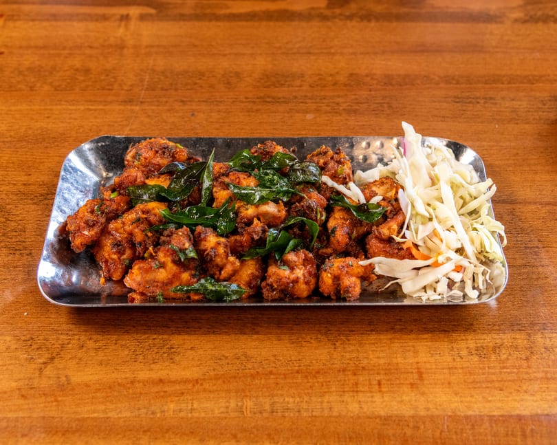 Crispy fried chicken pieces with green herbs and shredded cabbage on a silver platter.