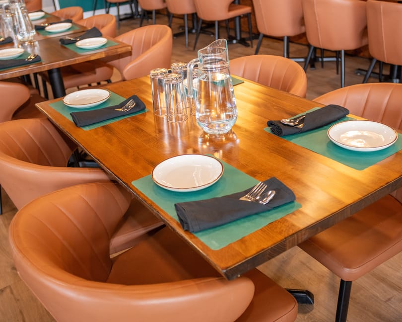 A restaurant dining room with wooden tables, brown leather chairs, and place settings with water pitchers.