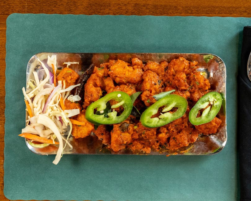 Overhead view of a metal tray filled with orange chicken, sliced green peppers, and a side salad.