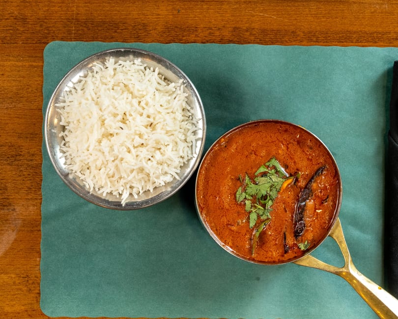 Overhead view of a bowl of white rice and a pot of red curry with cilantro.