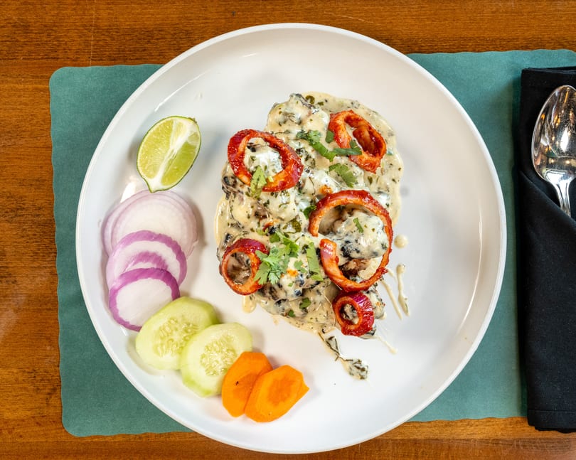 Creamy chicken dish with red onion rings, cilantro, and a side of sliced vegetables.