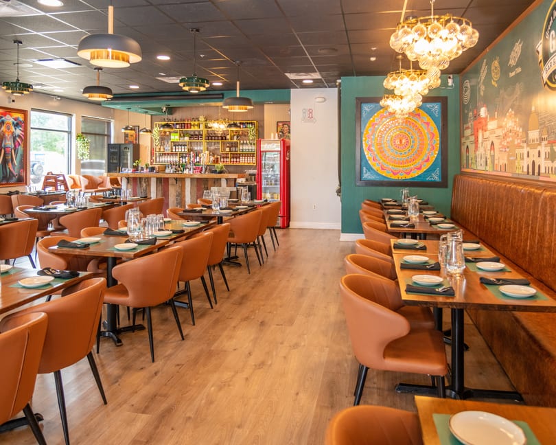 An empty restaurant dining room with brown chairs, wooden tables, a bar, and colorful wall art.