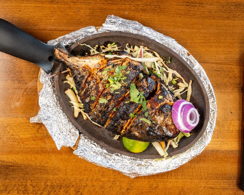Grilled whole fish with herbs, lime, and red onion on a sizzling platter with foil.