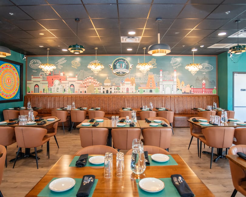 The Great Indian Food Bar & Kitchen dining room features a mural, brown booths, and set tables.