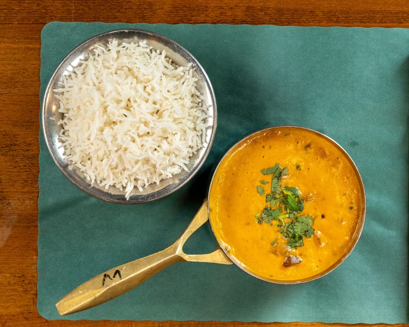 Overhead view of a bowl of white rice and a pot of yellow curry with cilantro on a green placemat.