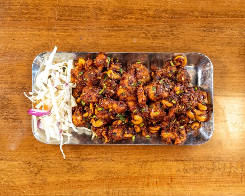 Spicy fried chicken with cashews and fresh cabbage salad on a metal tray.