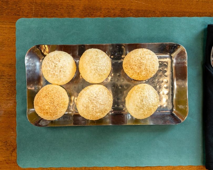 Six golden-brown pani puri shells arranged on a rectangular silver tray, on a green placemat.