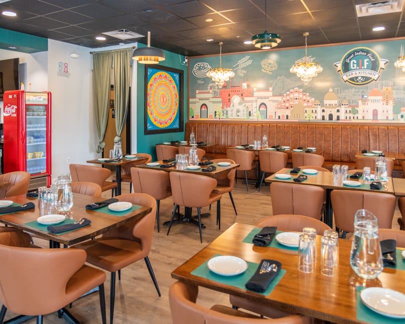 Interior of a Great Indian Food Bar & Kitchen dining room with tables, chairs, and a mural.