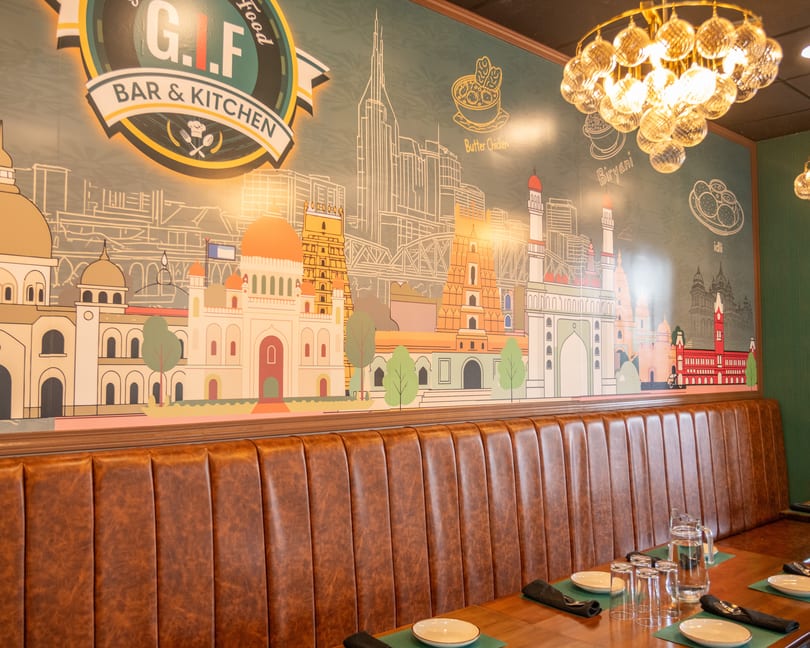 Restaurant interior with brown leather booth seating, set tables, and a mural of cityscapes and food.