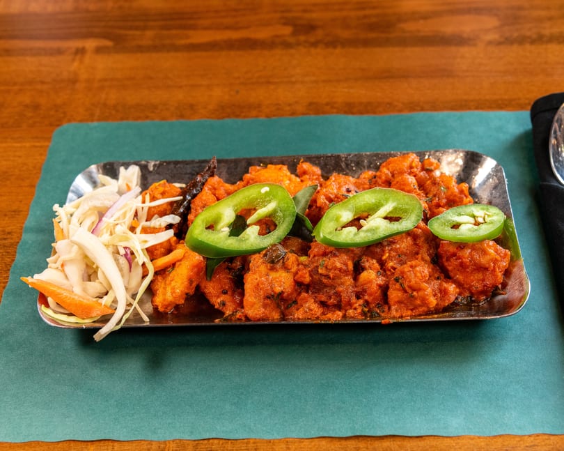 Spicy orange chicken dish with green peppers and a side of pickled vegetables on a metal tray.